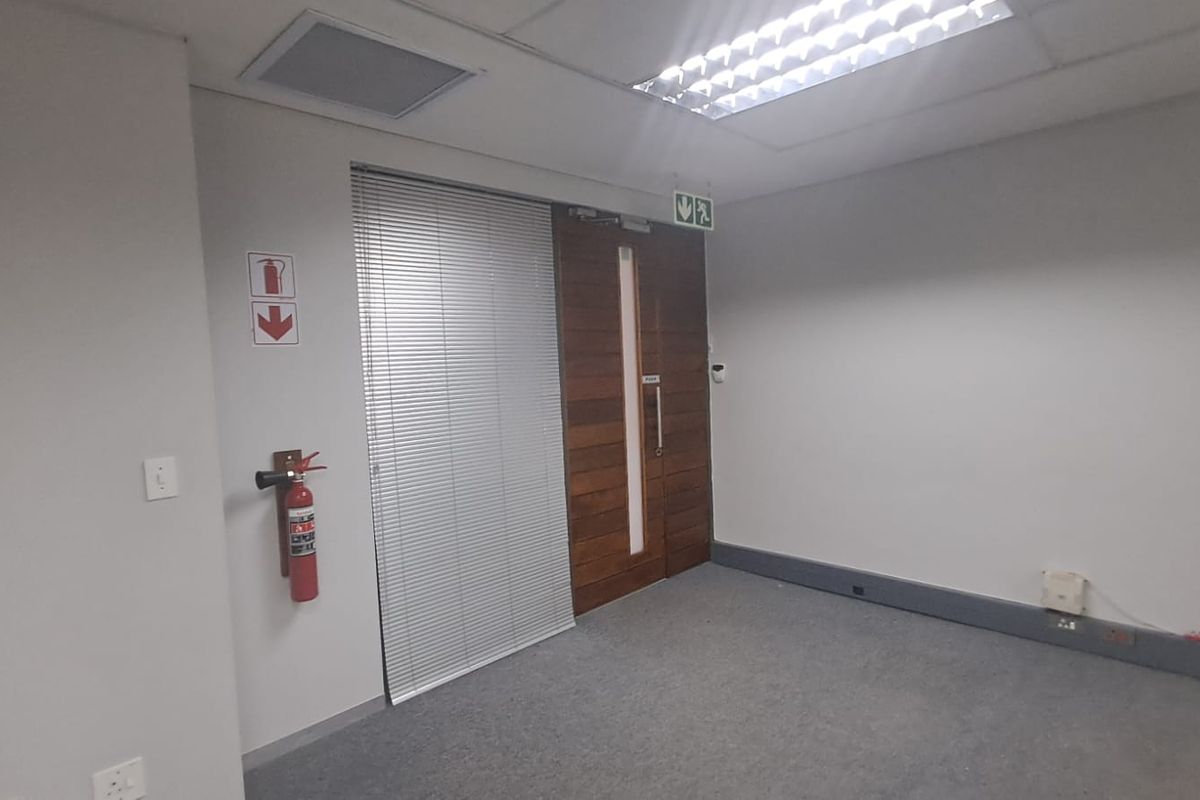 A vacant office space featuring carpeted flooring, a suspended ceiling with recessed lighting, and a solid timber entrance door.