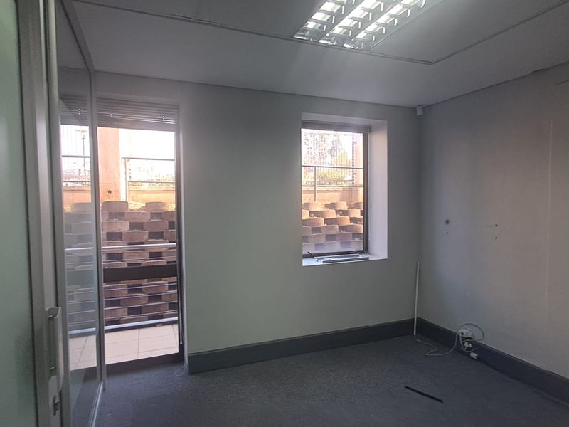 An empty office space featuring glass partitioning, recessed lighting, and carpeted flooring, suitable for a professional workspace.