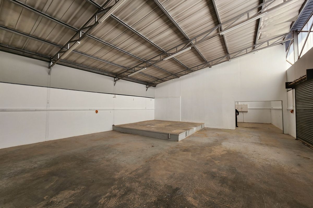 Spacious industrial utility area featuring exposed steel roof trusses, concrete flooring, a raised platform, and a functional roller shutter door.