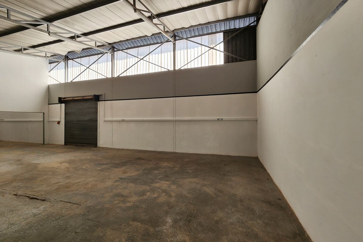 Spacious industrial utility area featuring high ceilings with exposed steel trusses, concrete flooring, and a secure roller shutter door.