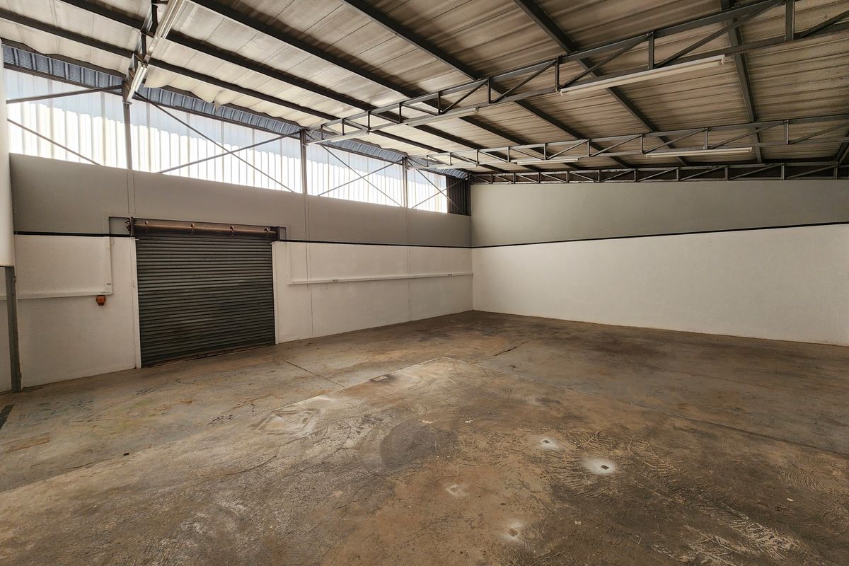 Spacious industrial utility area featuring high ceilings with exposed steel trusses, a large roller shutter door, and durable concrete flooring.