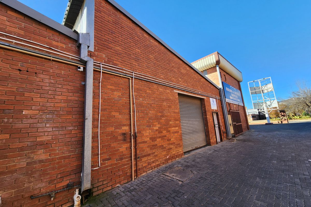 Rear exterior view of an industrial property featuring a brick facade, roller shutter door, and paved access area.