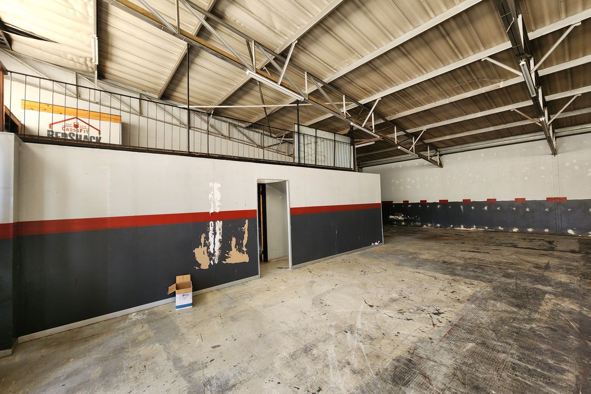Spacious industrial utility area featuring exposed steel roof trusses, a mezzanine level, and concrete flooring, suitable for workshop or storage use.