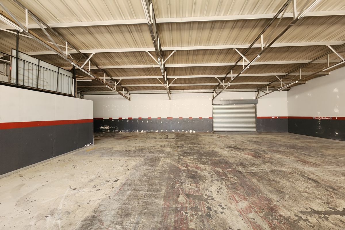 Spacious industrial warehouse unit featuring high exposed steel roof trusses, a large roller shutter door, and a mezzanine level, ideal for storage or workshop use.