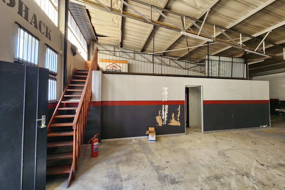 Industrial utility space featuring a mezzanine level, metal staircase, exposed steel roof trusses, and concrete flooring, suitable for storage or workshop use.