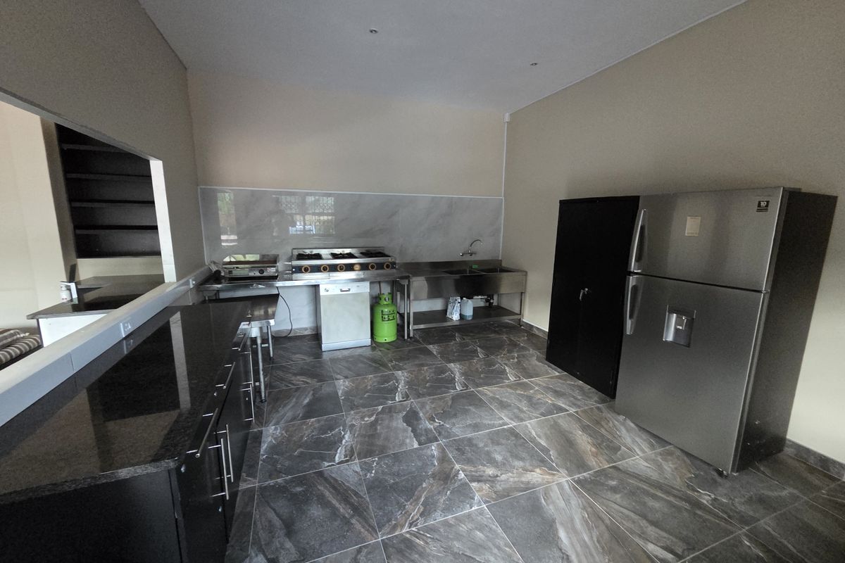 A modern kitchen area featuring dark granite countertops, stainless steel commercial-style sink and gas hob, marble-look wall tiles, and large format floor tiling.