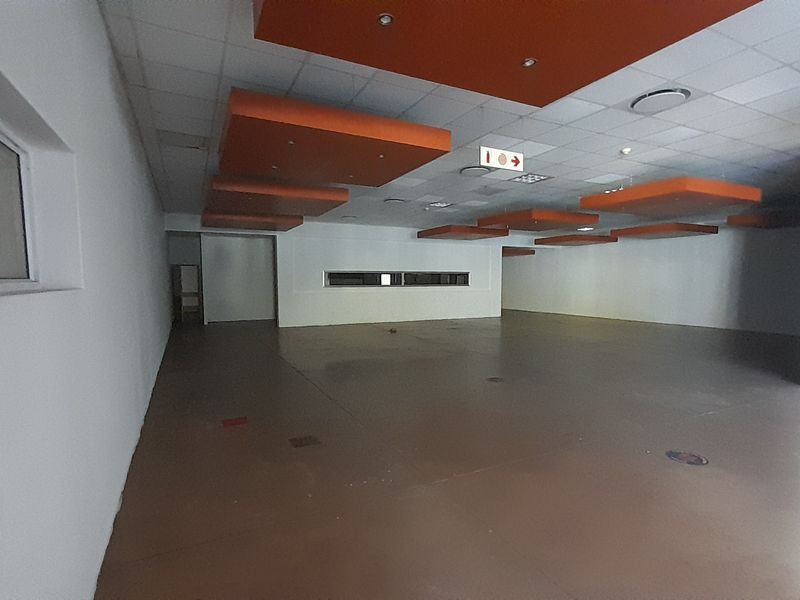 A spacious, open-plan retail area featuring polished concrete floors, a suspended ceiling with decorative orange bulkheads, and recessed lighting throughout.