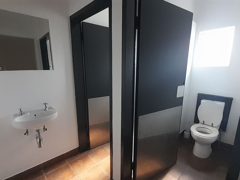 A clean, functional commercial bathroom featuring a wall-mounted basin, a private toilet cubicle, and tiled flooring.