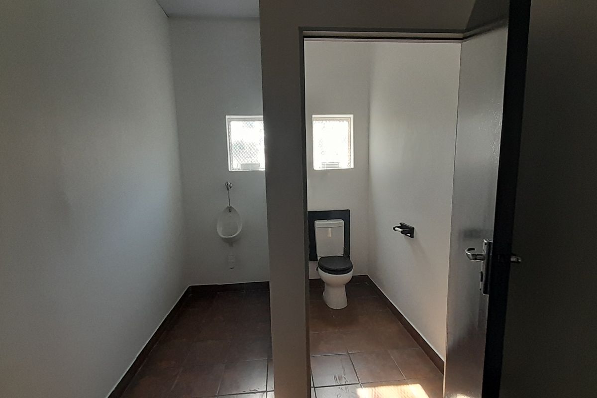 A functional commercial bathroom facility featuring a private toilet cubicle and a wall-mounted urinal with tiled flooring.