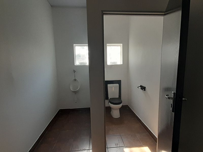 A functional commercial bathroom facility featuring a private toilet cubicle and a wall-mounted urinal with tiled flooring.