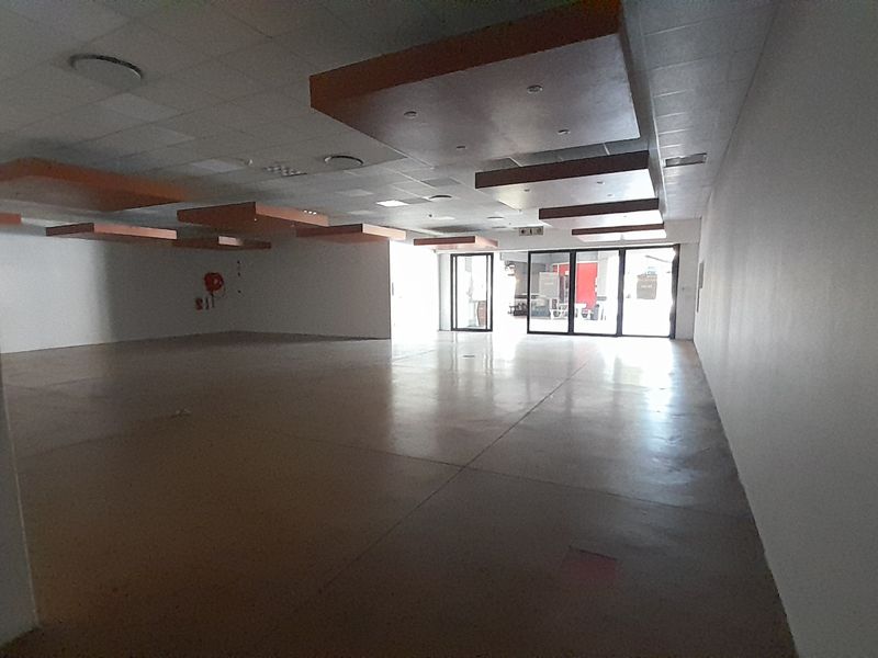 Spacious open-plan retail unit featuring polished concrete floors, a modern suspended ceiling with recessed lighting, and large glass entrance doors.