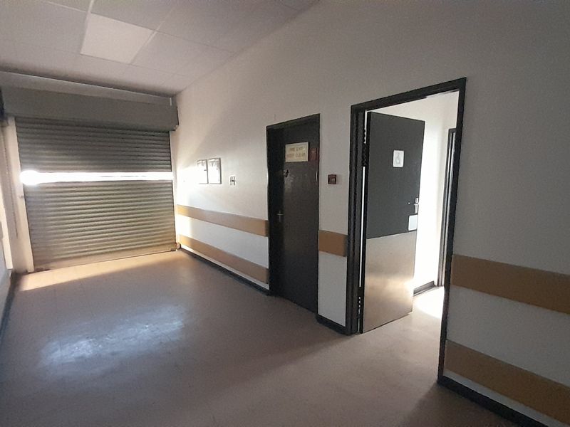 A functional commercial hallway featuring a roller shutter door, fire safety equipment, and protective wall guards, leading to an accessible restroom.