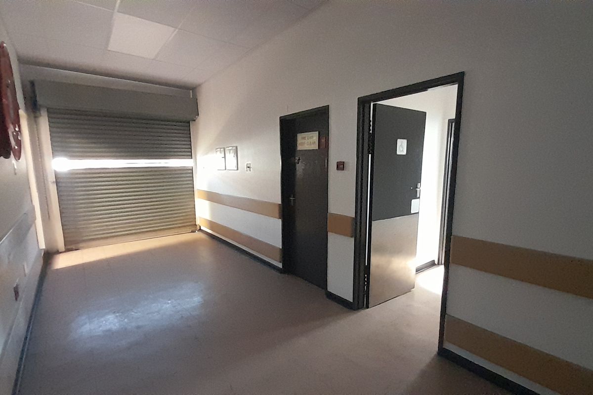A functional commercial hallway featuring a roller shutter door, fire safety equipment, and protective wall guards, leading to an accessible restroom.