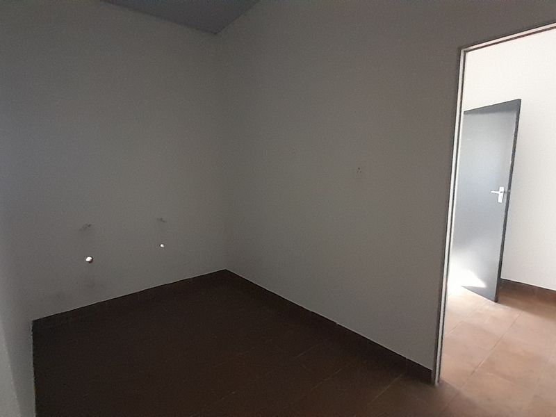 An empty utility or service room featuring tiled flooring and visible plumbing connections, providing a functional space for laundry or storage needs.