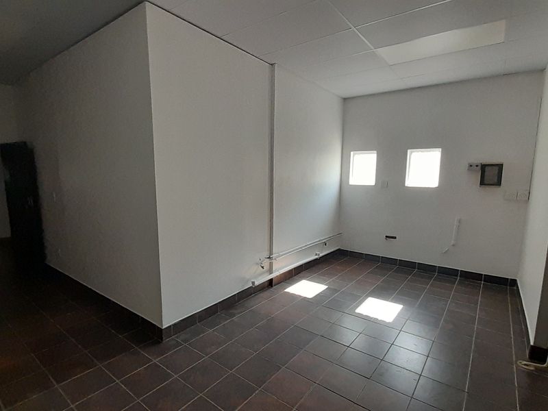An empty, functional utility space featuring tiled flooring, a suspended ceiling, and exposed conduit, suitable for various commercial or storage purposes.