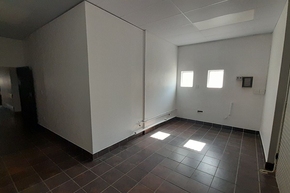 An empty, functional utility space featuring tiled flooring, a suspended ceiling, and exposed conduit, suitable for various commercial or storage purposes.