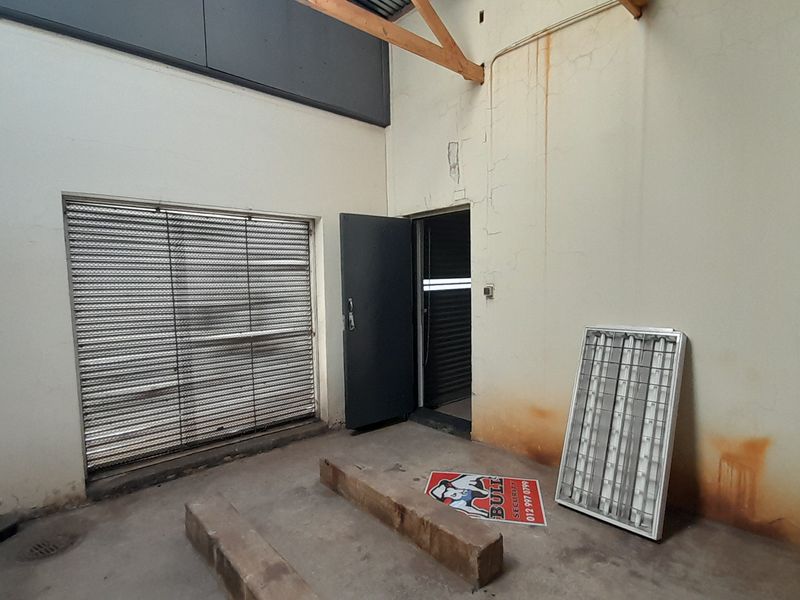 An empty utility space featuring concrete flooring, a roller shutter door, and exposed timber roof trusses, showing signs of wall staining and wear.