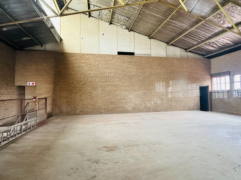 Spacious industrial utility area featuring exposed brick walls, high-pitched metal roofing, and concrete flooring, suitable for storage or workshop use.