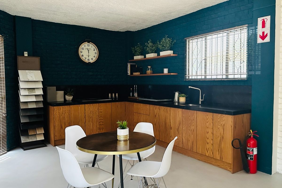 A modern kitchen area featuring wooden cabinetry, black stone countertops, floating shelves, and painted brick walls, creating a stylish and functional workspace.