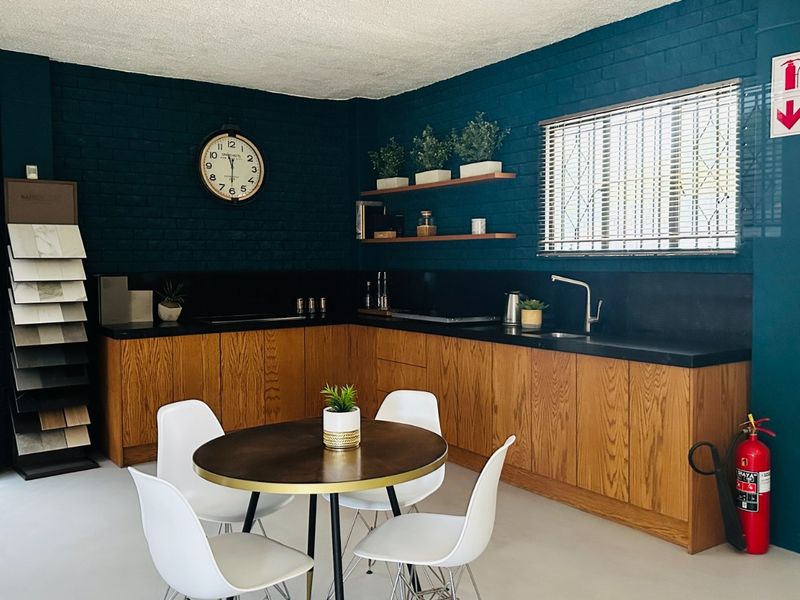 A modern kitchen area featuring wooden cabinetry, black stone countertops, floating shelves, and painted brick walls, creating a stylish and functional workspace.