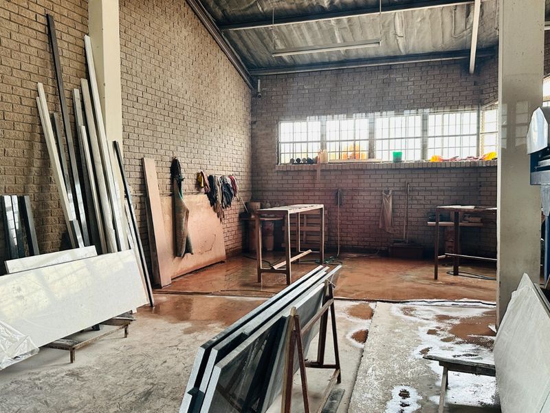 Industrial workshop space featuring exposed brick walls, concrete flooring, and high-ceiling steel structure, suitable for manufacturing or heavy-duty storage operations.