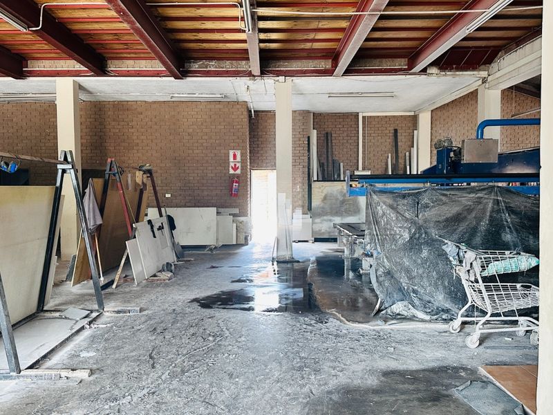 Industrial utility space featuring exposed steel beams, brick walls, and concrete flooring, currently utilized for heavy machinery and storage.