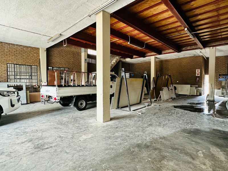 Spacious industrial garage or workshop area featuring exposed brick walls, steel beam ceiling structure, and durable concrete flooring.