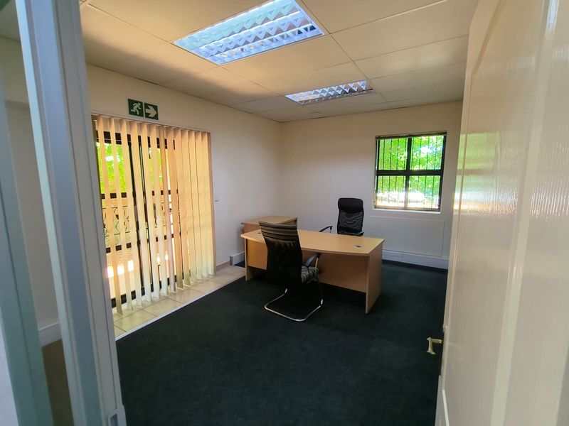 A functional office space featuring carpet flooring, recessed fluorescent lighting, and vertical blinds, providing a professional environment with natural light.
