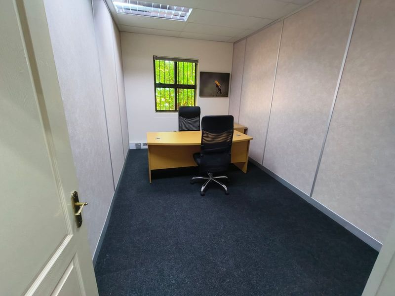 A functional office space featuring carpeted flooring, partition walls, and a window with security bars, providing a professional work environment.