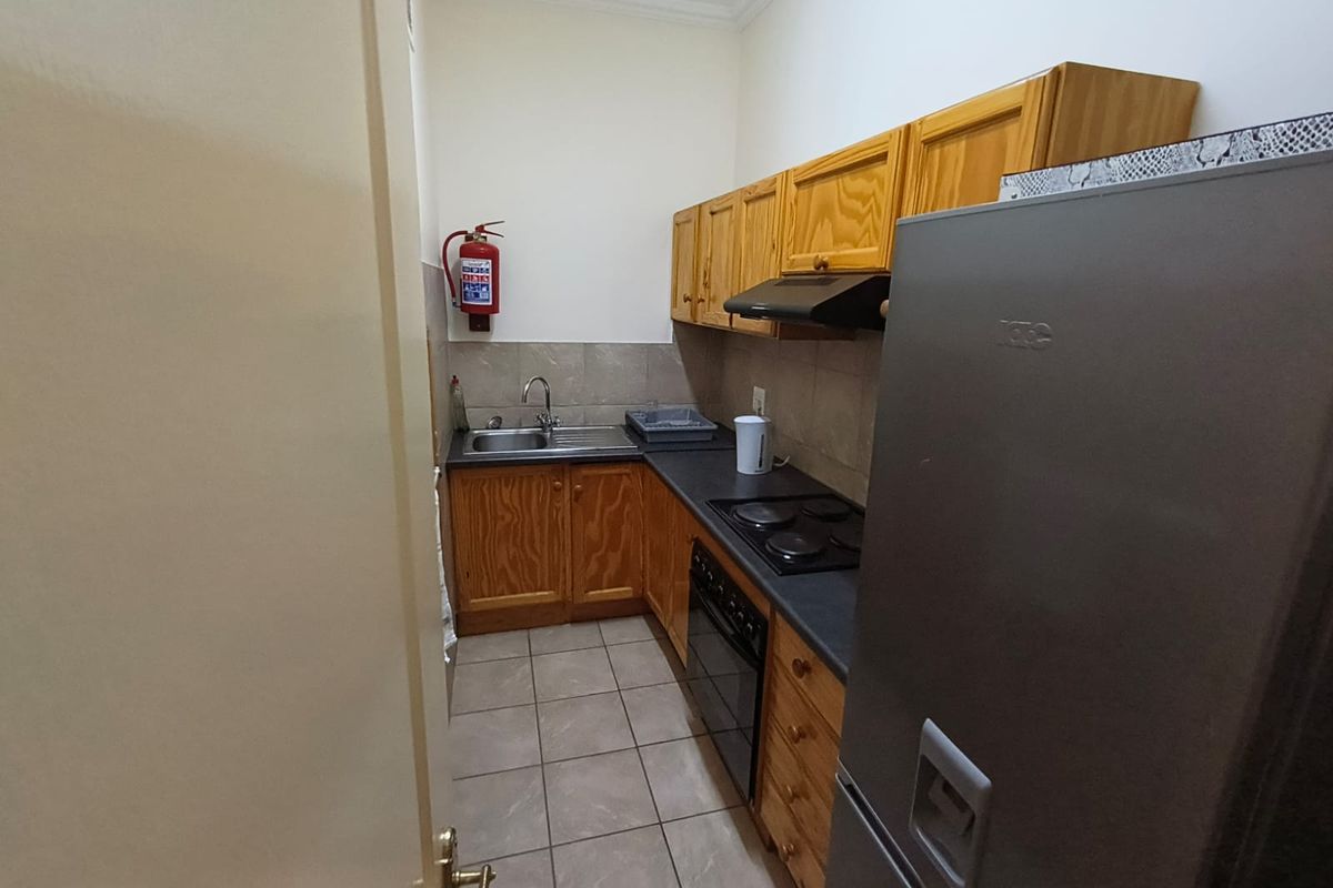 Compact office kitchenette featuring wooden cabinetry, laminate countertops, built-in electric hob, oven, extractor fan, and tiled flooring.