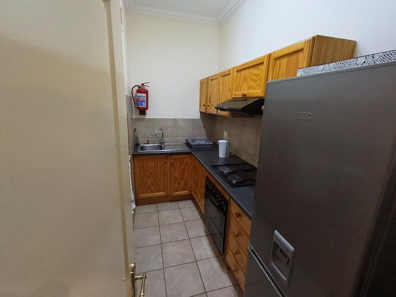 Compact office kitchenette featuring wooden cabinetry, laminate countertops, built-in electric hob, oven, extractor fan, and tiled flooring.