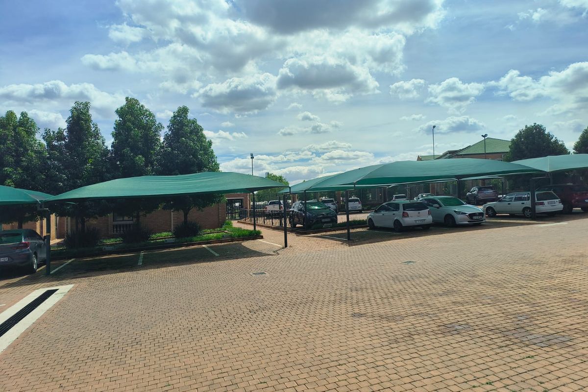 A paved office parking area featuring multiple shade cloth carports and secure perimeter fencing.