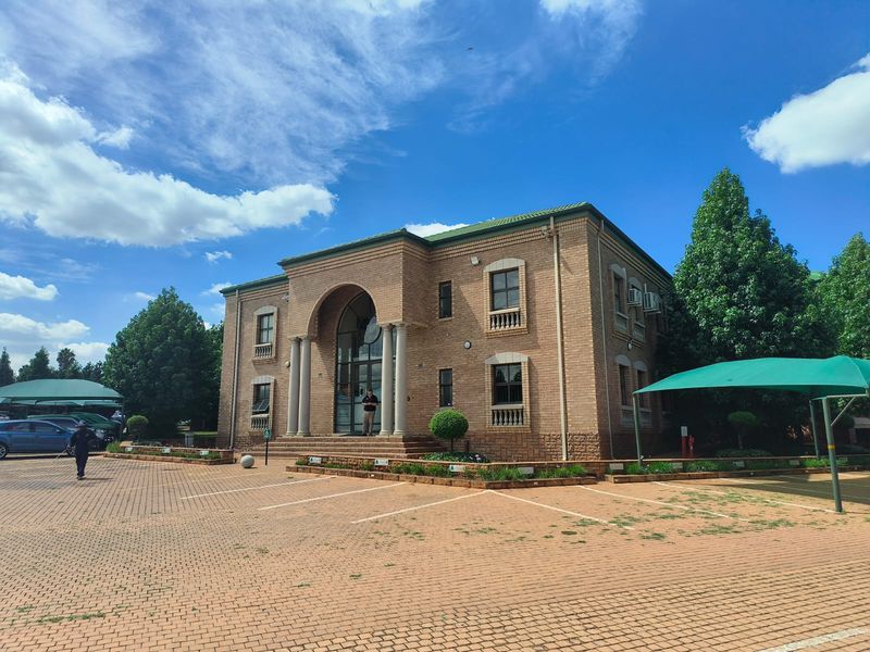 A professional office building featuring a classic brick facade, arched entrance with columns, and an extensive paved parking area with shade cloth carports.