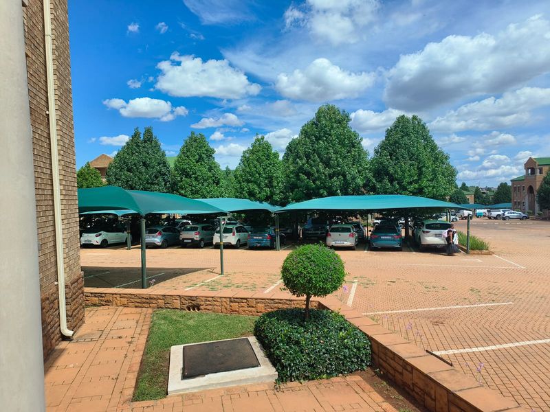 A paved outdoor parking area featuring multiple shade cloth carports and landscaped retaining walls.