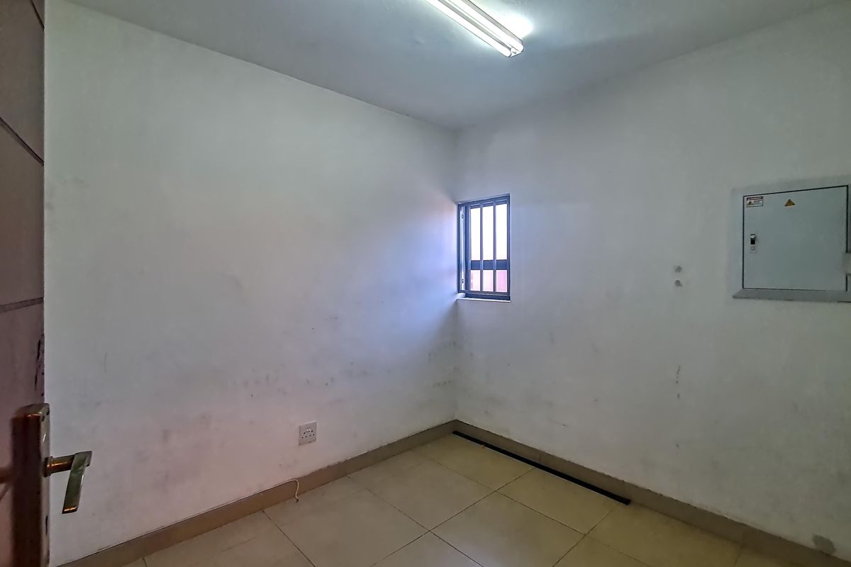 A small, empty utility room featuring tiled flooring, a security-barred window, and a wall-mounted electrical distribution board.