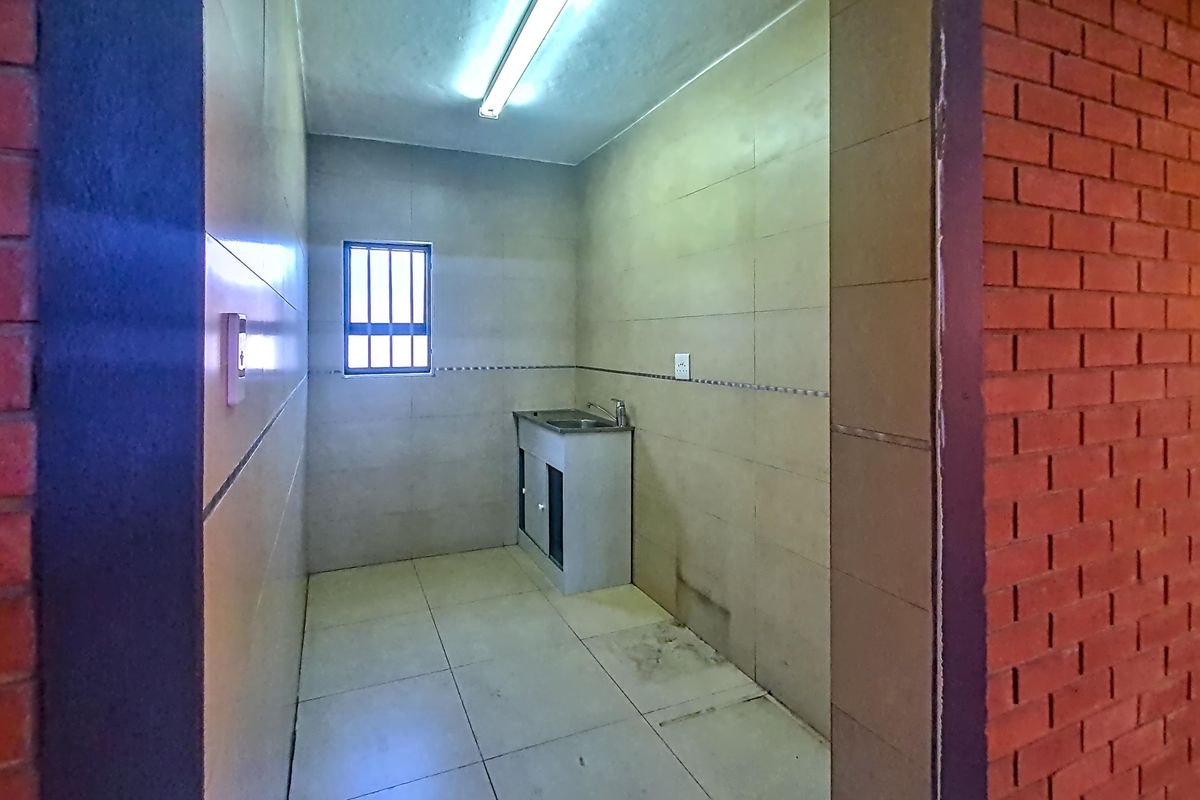 A functional scullery or utility area featuring tiled walls and flooring, a stainless steel sink, and a window with security bars.