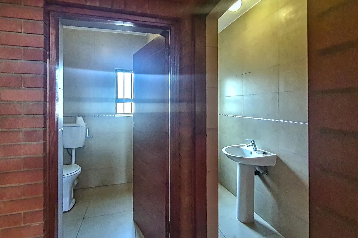 A functional bathroom featuring a pedestal sink and toilet, with tiled walls and flooring, set against an exposed brick interior wall.