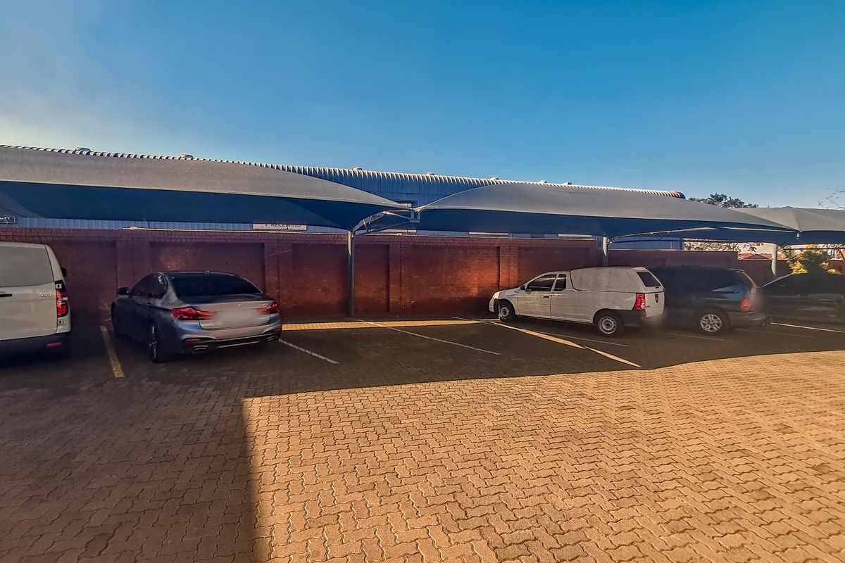 Industrial property exterior featuring a paved parking area with shade cloth structures and a brick boundary wall.