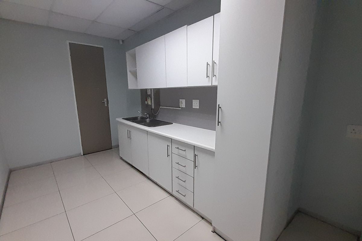 A clean, functional office kitchenette featuring white built-in cabinetry, a stainless steel sink, and neutral tiled flooring.