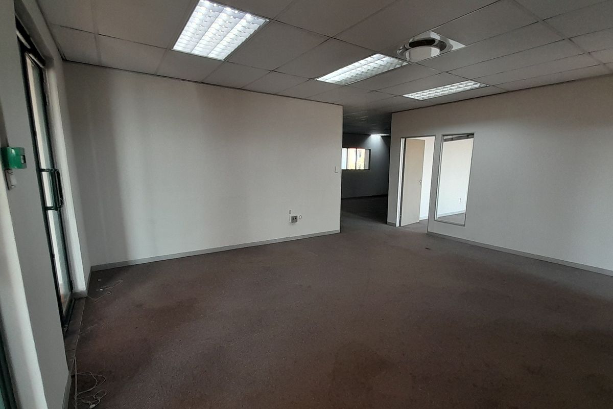 An empty, open-plan office space featuring a suspended ceiling with recessed lighting, carpeted flooring, and an internal glass partition.