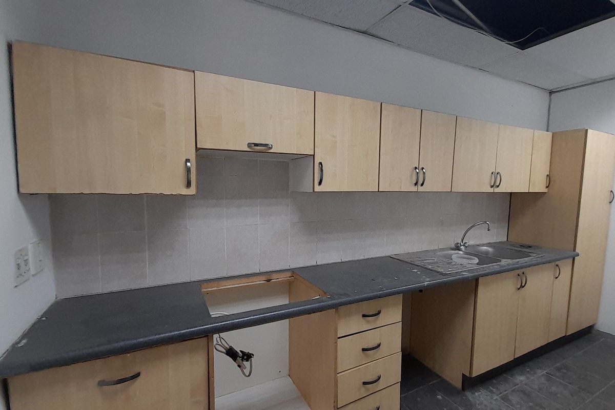 A functional office kitchenette featuring laminate cabinetry, a stainless steel sink, and tiled splashback, currently requiring maintenance and appliance installation.