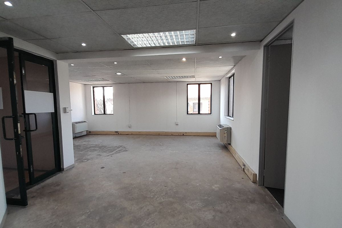 An empty, open-plan office space featuring a suspended ceiling, recessed lighting, air conditioning units, and large windows, currently requiring flooring and finishing work.