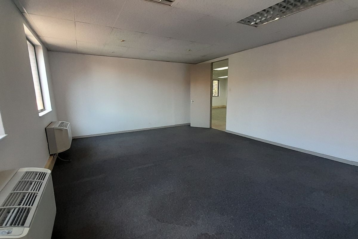 An empty office space featuring a suspended ceiling with recessed lighting, carpeted flooring, and wall-mounted air conditioning units.