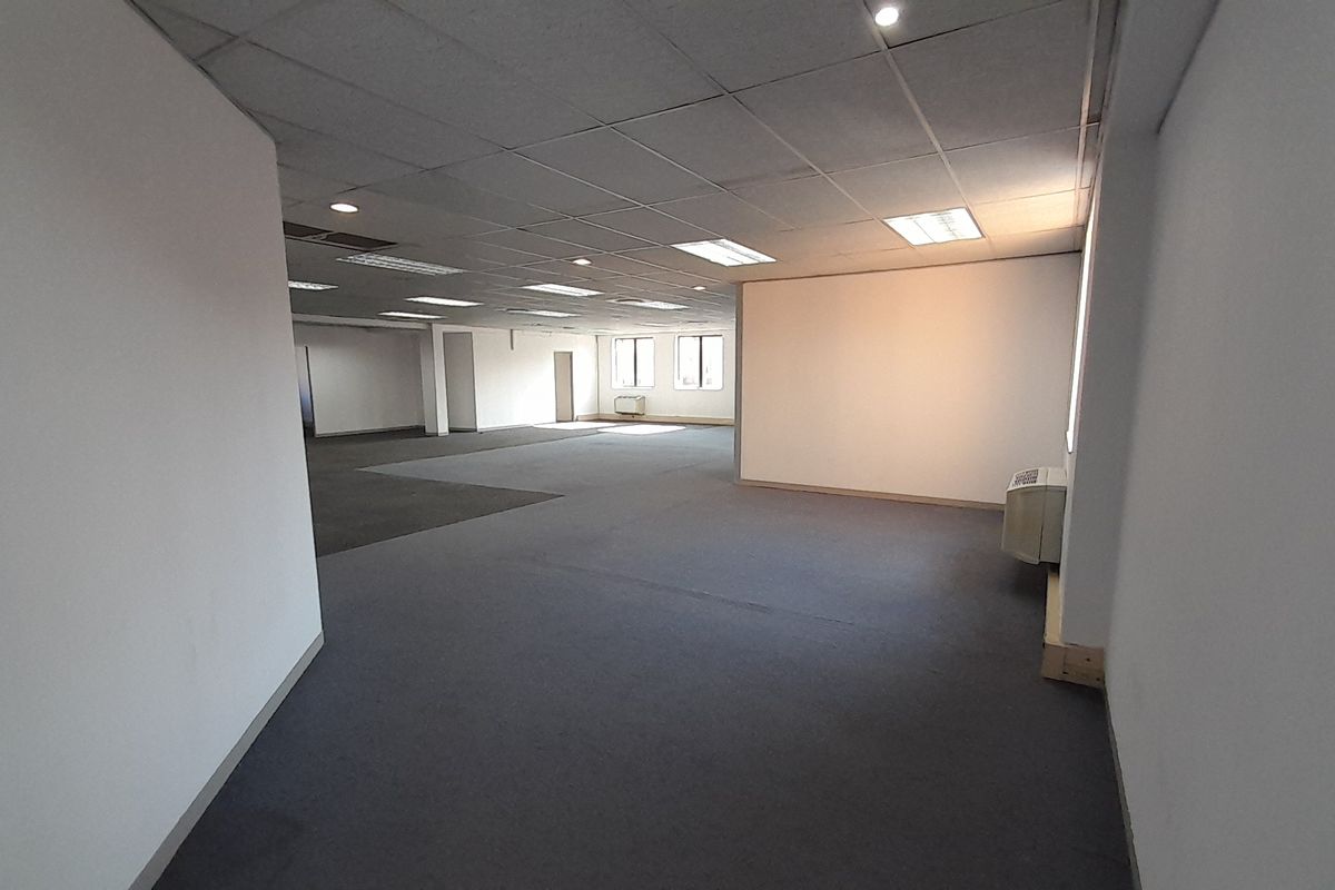 A spacious, open-plan office area featuring neutral carpeting, a suspended ceiling with recessed lighting, and an integrated air conditioning unit.