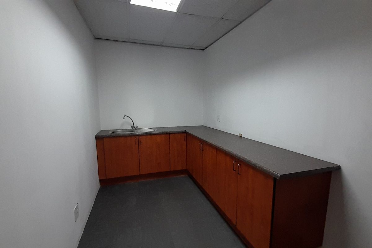 A functional utility space featuring built-in wooden cabinetry, a laminate countertop, and a stainless steel sink, suitable for office kitchenette or storage use.