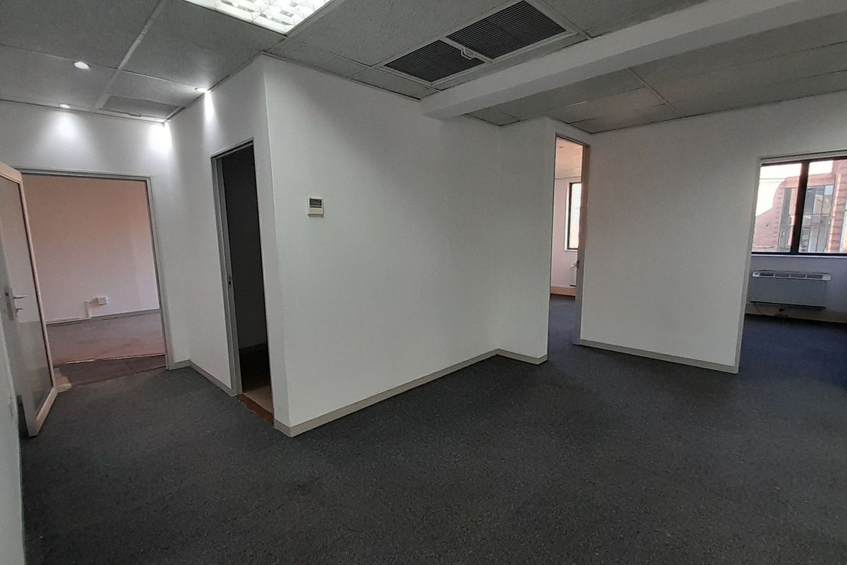 An empty office suite featuring neutral walls, carpeted flooring, suspended ceilings with recessed lighting, and multiple doorways leading to adjacent workspaces.