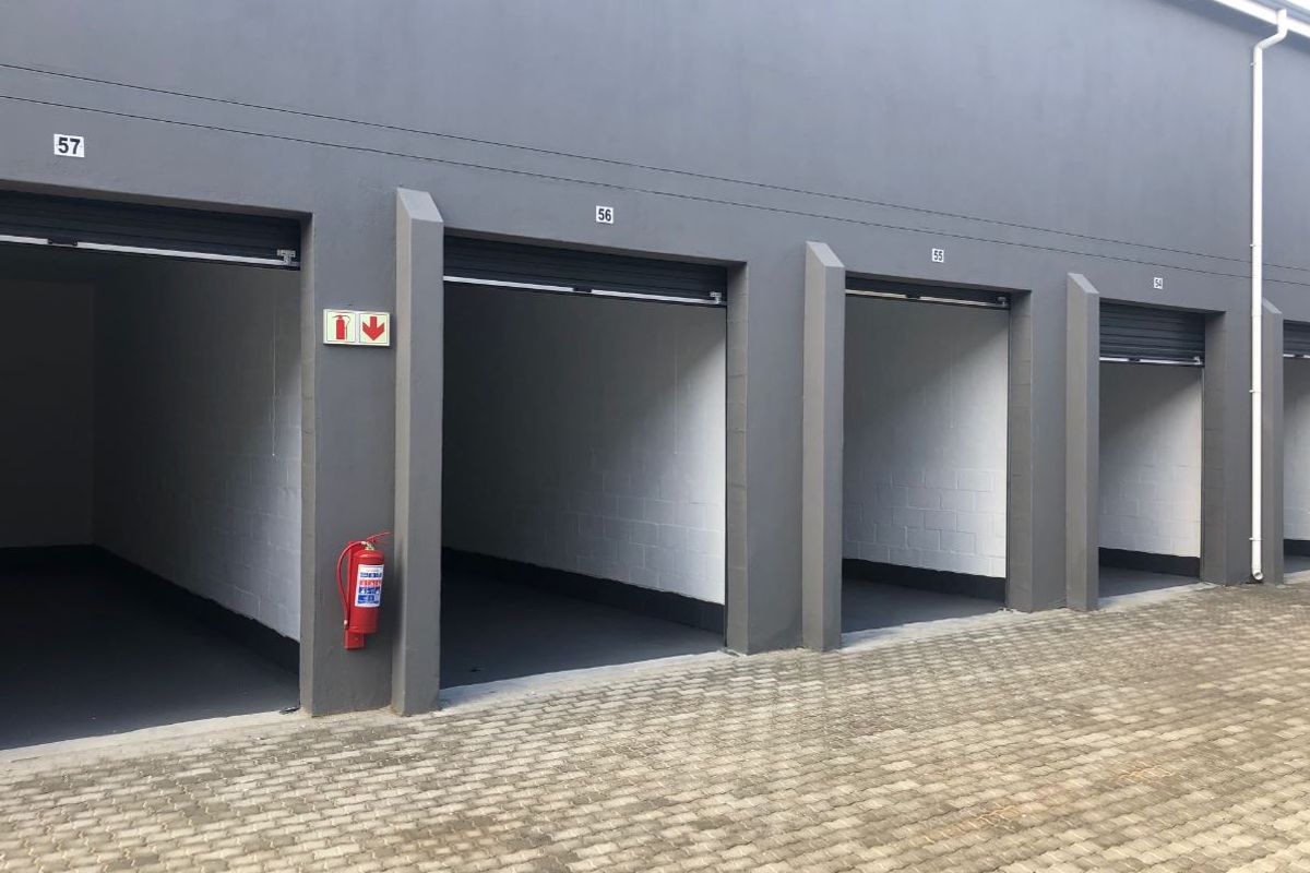 A row of modern, well-maintained industrial garage units featuring roller shutter doors, painted masonry walls, and a paved exterior driveway.