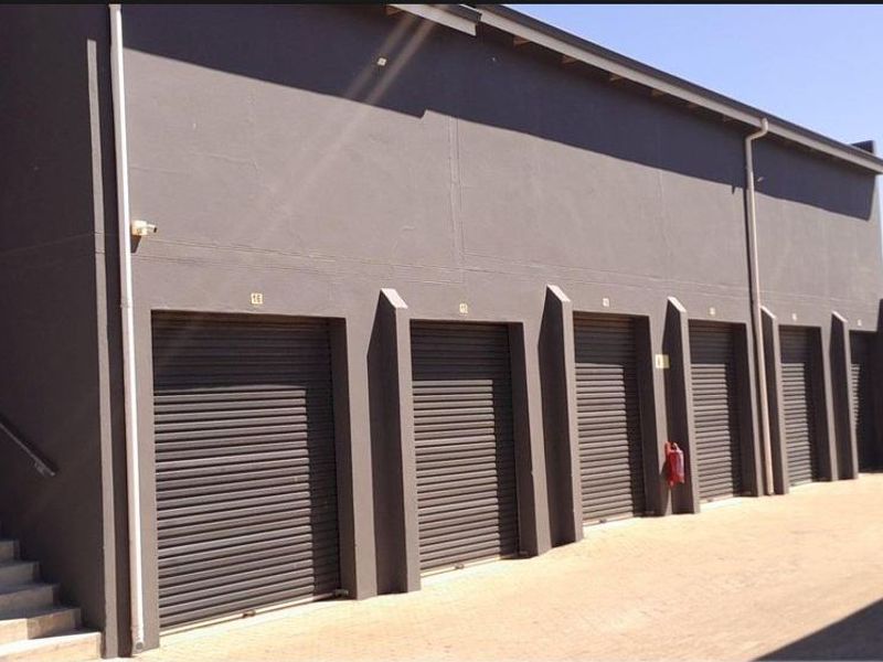 Industrial storage facility featuring multiple roller shutter doors, an external staircase, and secure perimeter fencing.