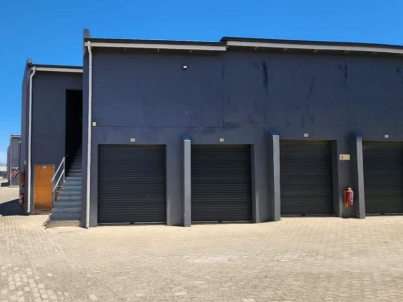 Industrial property exterior featuring multiple roller shutter doors, paved driveway access, and an external staircase leading to an upper level.