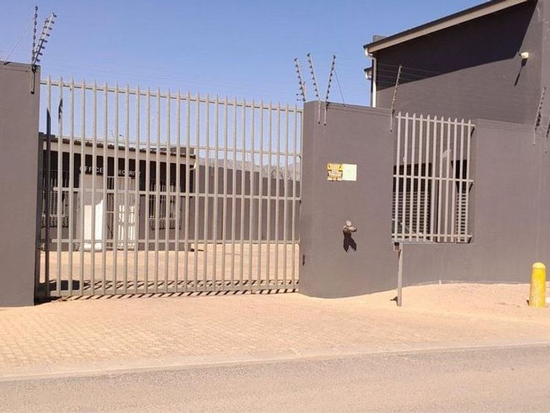 Secure industrial property entrance featuring a gated driveway, perimeter wall with electric fencing, and paved access area.